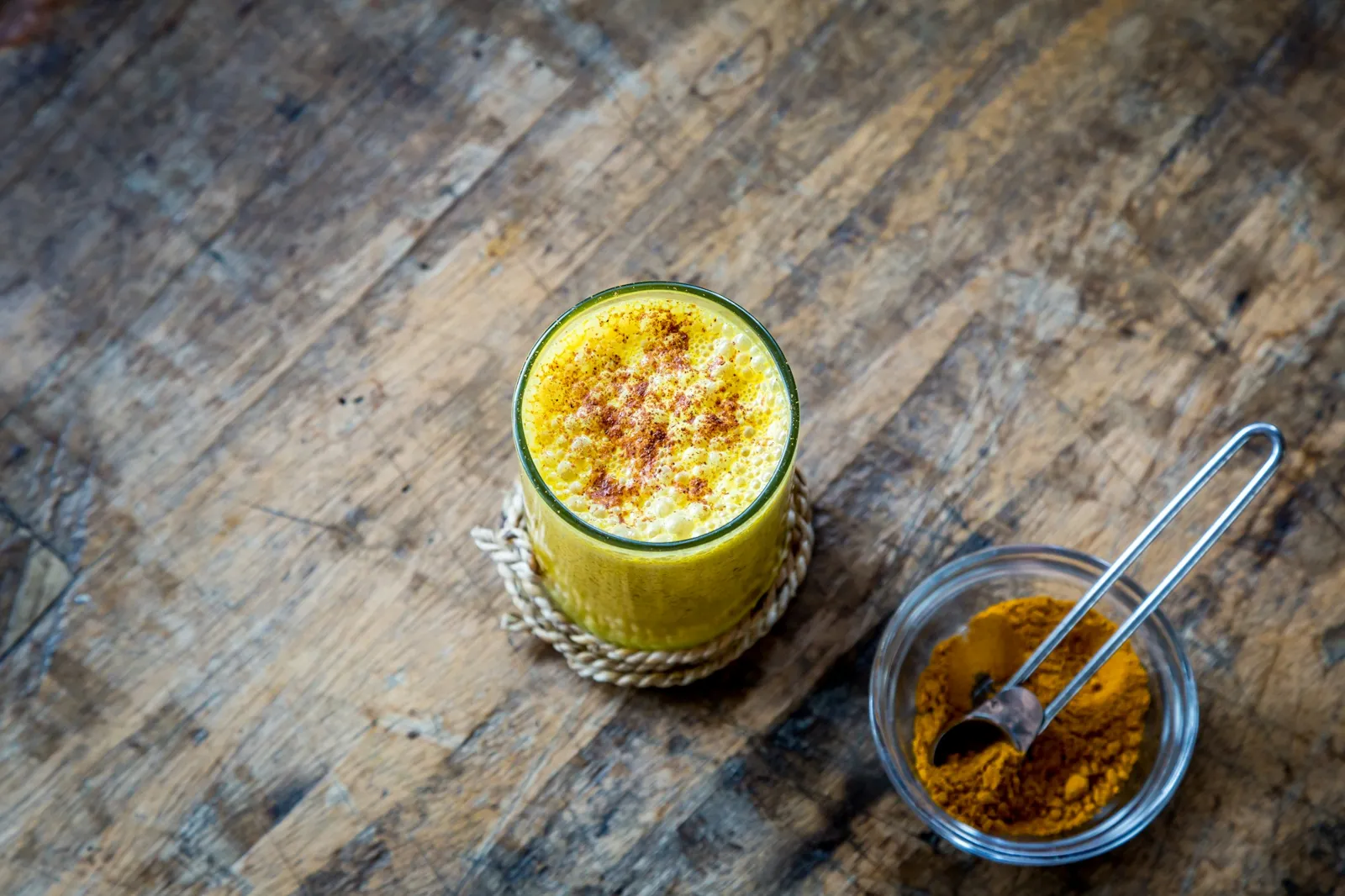 A glass of golden milk next to a strainer of turmeric
