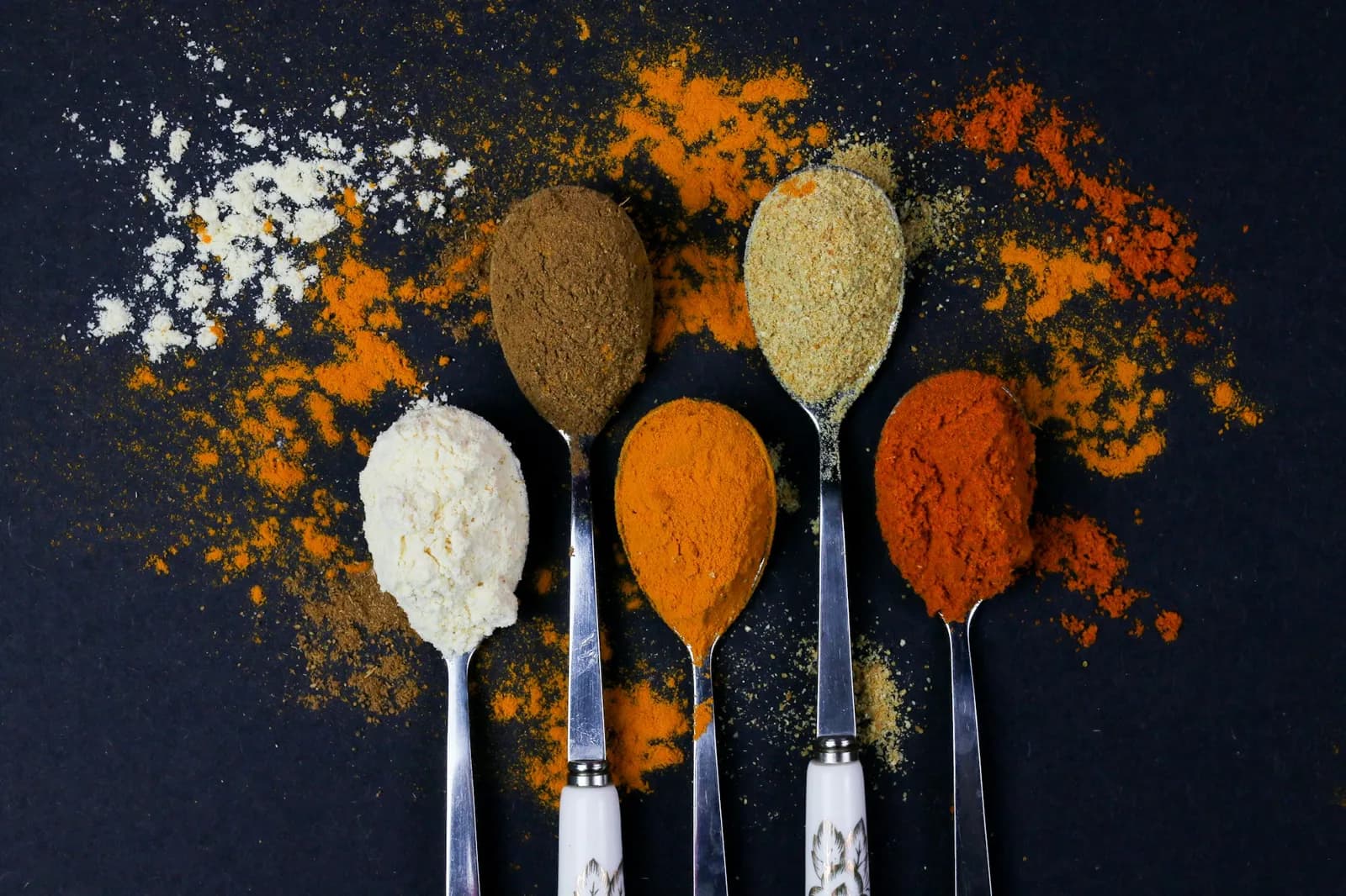 Spoons of ground spices on a dark table